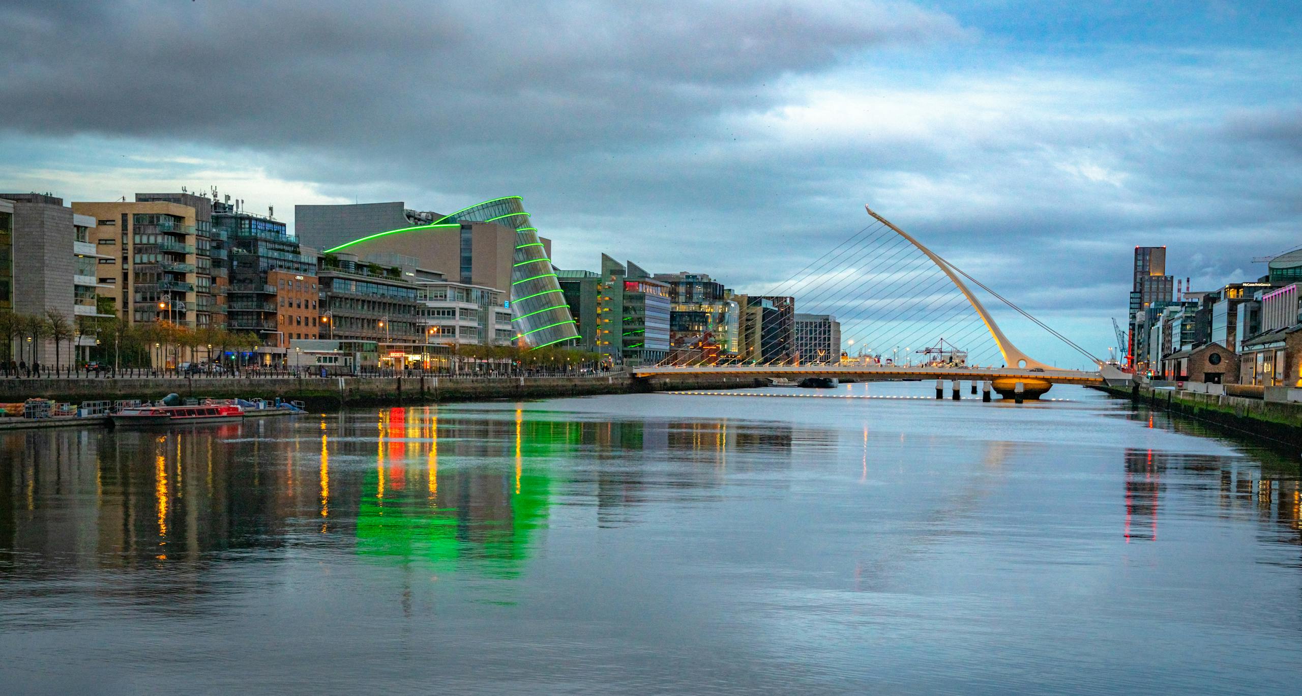 Scenic view of Samuel Beckett Bridge and modern Dublin skyline reflecting in River Liffey at twilight.